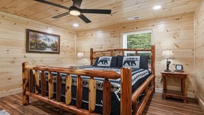 Ein Schlafzimmer einer Holzhütte mit einem Bett, einem Deckenventilator, einem Fenster und einem Bild an der Wand.