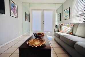 A living room with a sofa, a coffee table with a bowl and a woven tray, and framed artwork on the walls. - Welcome to Shipyard Unit 155, a charming 2-bedroom, 1-bath ground-level condo located in the desirable Truman Annex community, just two blocks from Duval Street. This convenient Key West is within easy walking distance of the Truman Waterfront. (Key West)