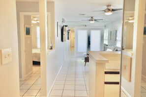 A hallway with a ceiling fan, a kitchen area with a counter, and a door leading to another room. - Welcome to Shipyard Unit 155, a charming 2-bedroom, 1-bath ground-level condo located in the desirable Truman Annex community, just two blocks from Duval Street. This convenient Key West is within easy walking distance of the Truman Waterfront. (Key West)