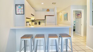 Una cocina moderna con una isla central, taburetes de bar y un reloj en la pared.