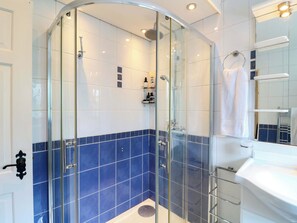 Ein modernes Badezimmer mit einer in Glas abgeschlossenen Dusche, blauen Fliesenwänden, einem weißen Waschbecken und einem Spiegel darüber.