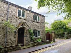 A stone house with a dark entrance, a small porch, and a gated driveway. - The Chimes (Hope Valley)