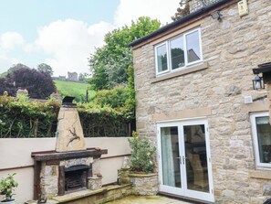A stone building with a fireplace, a large glass door, and a view of a hill with a castle. - The Chimes (Hope Valley)