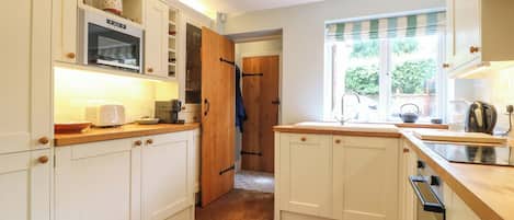 A kitchen with white cabinets, a microwave, and a window with blinds.