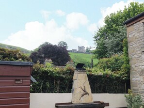 A stone wall with a deer sculpture, a wooden building, and a view of a castle on a hill. - The Chimes (Hope Valley)