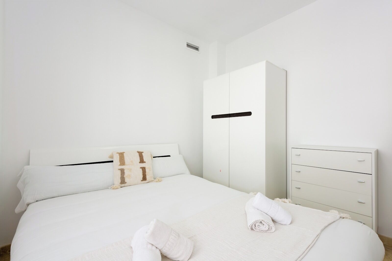 Een slaapkamer met een bed, een kledingkast en een dressoir.