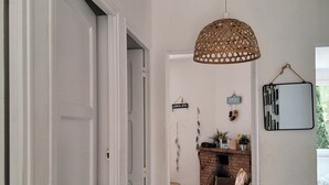 Un corridoio con una porta bianca, un lampadario intrecciato a sospensione, un camino in mattoni e uno specchio fissato al muro.
