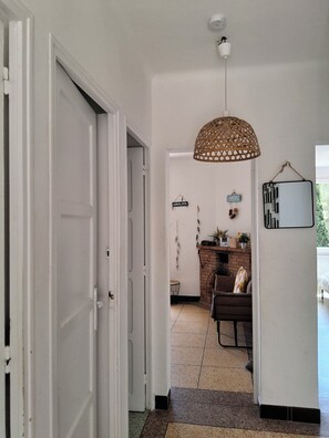 A hallway with a white door, a hanging woven light fixture, a brick fireplace, and a wall-mounted mirror. - Family home on the port of Le Niel (Hyères)