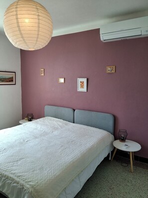 Ein Schlafzimmer mit einem großen Bett, einem grauen Kopfteil, einem runden Nachttisch und einer wandmontierten Klimaanlage.