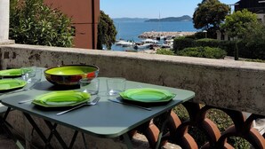 Un tavolo apparecchiato con piatti e bicchieri verdi, con vista su un porto turistico con barche e una spiaggia in lontananza.