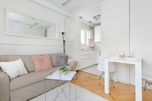 Ein modernes Wohnzimmer mit einer Couch, einem kleinen Tisch mit Pflanze, einem weißen Schreibtisch und einem großen Spiegel.