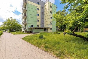 Een meerlaags woongebouw met een groene gevel, een geplaveid pad en omliggend groen.