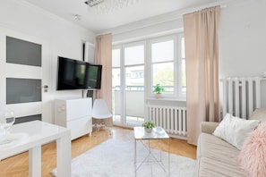 Een moderne woonkamer met een televisie, witte meubels, een bank, een bijzettafeltje en een plant.