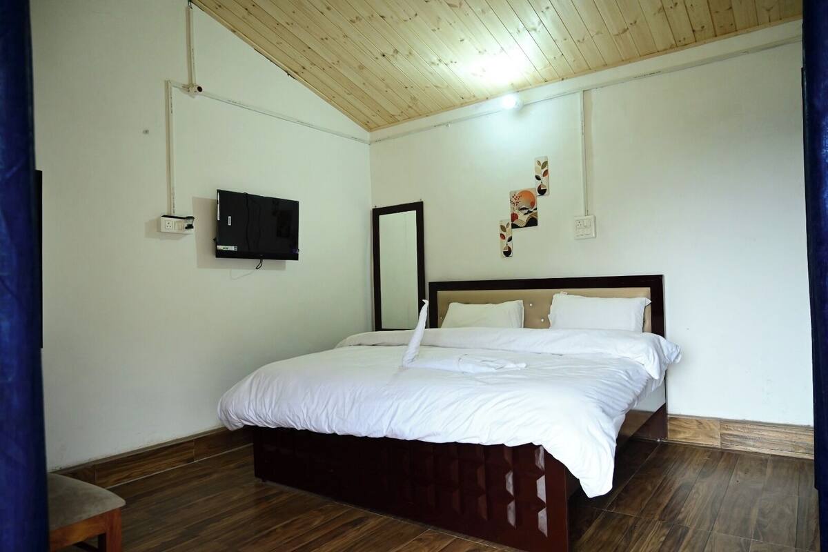 A bedroom with a wooden ceiling, a bed with white bedding, a flat-screen TV mounted on the wall, and a small table.