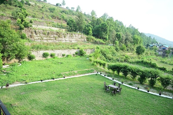 A grassy outdoor area with a table and chairs, surrounded by trees and a stone wall. - Blue Sky Homestay (Nainital)