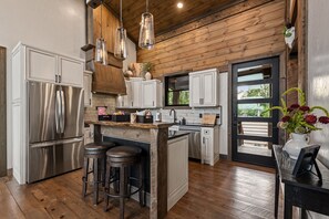 A modern kitchen with a central island, stainless steel appliances, and wooden flooring. - 6 Acre Summit: High-End Escape • Pool • HotTub • FirePit • Creek Access • Games (Epworth)
