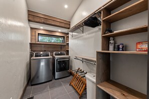 A compact laundry room with two stainless steel washers, a dryer, and a wooden shelf with cleaning supplies. - 6 Acre Summit: High-End Escape • Pool • HotTub • FirePit • Creek Access • Games (Epworth)