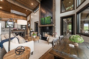A spacious living area with a fireplace, a dining table, and a kitchen in the background. - 6 Acre Summit: High-End Escape • Pool • HotTub • FirePit • Creek Access • Games (Epworth)