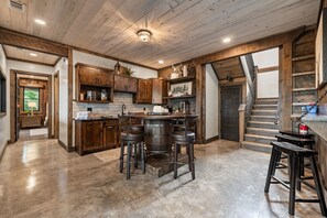 Eine rustikale Küche mit Holzsäulen, einer zentralen Kochinsel mit Sitzgelegenheiten und einer Treppe zu einer weiteren Ebene.
