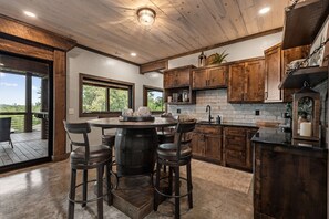 Eine moderne Küche mit Holzschränken, einer zentralen Kochinsel mit Barhocker und großen Fenstern.