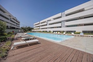 Ein modernes Gebäude mit Schwimmbad, Liegestühlen und einer Holzterrasse.