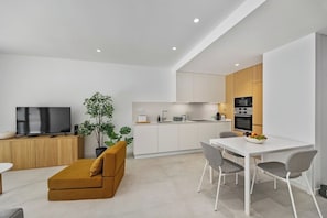 Ein stilvoller Wohnraum mit Sofa, Esstisch, Stühlen, Fernseher, Pflanze und Küchenbereich.