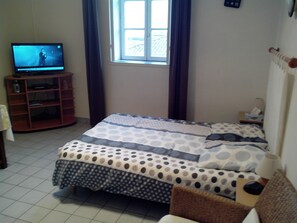 Ein Schlafzimmer mit Bett, Fernseher, Fenster und Holzschrank.
