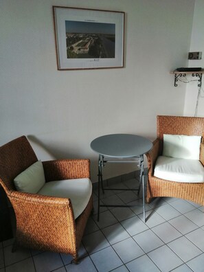 Ein Zimmer mit zwei Korbstühlen, einem kleinen runden Tisch und einem gerahmten Bild an der Wand.