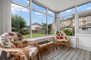 A sunroom with wicker furniture, large windows, and a view of a residential area. - Coldside House - Well Connected Dundee Stay (Dundee)