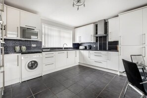 A modern kitchen with white cabinets, a built-in washing machine, a microwave, and a coffee maker. - Coldside House - Well Connected Dundee Stay (Dundee)
