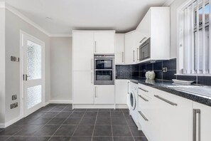 A modern kitchen with white cabinets, a double oven, a washing machine, and a black countertop. - Coldside House - Well Connected Dundee Stay (Dundee)