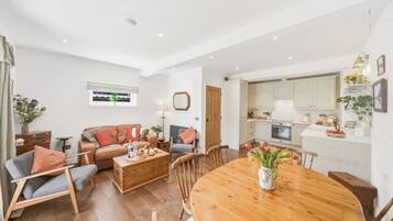 A spacious living area with a wooden dining table, a leather sofa, and a kitchen with white cabinets.