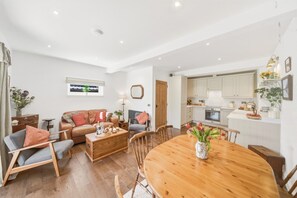 A spacious living area with a wooden dining table, a leather sofa, and a kitchen with white cabinets. - 20 Applegrove - Home from Home in Monifieth (Monifieth)