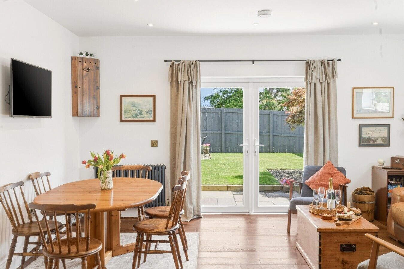 A dining area with a round table and chairs, a TV mounted on the wall, and a sliding glass door leading to a backyard.