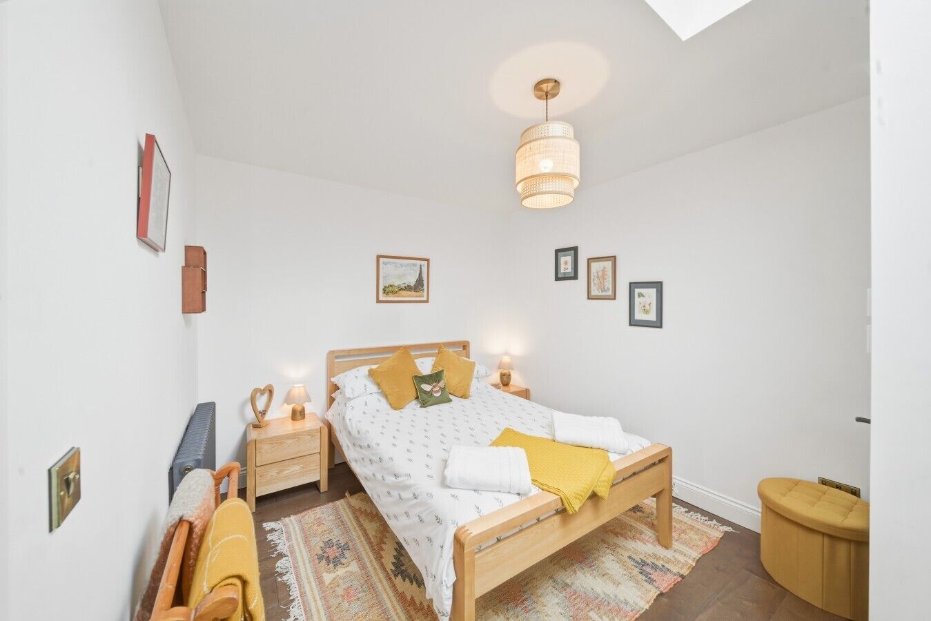 A bedroom with a bed, bedside tables, a hanging light fixture, and a window.