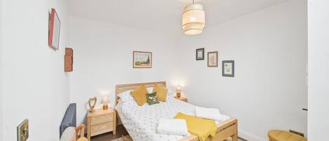 A bedroom with a bed, bedside tables, a hanging light fixture, and a window.