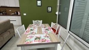 Ein Essbereich mit einem Tisch, gedeckt für vier Personen, umgeben von weißen Stühlen, einer grünen Wand und gerahmten Bildern.