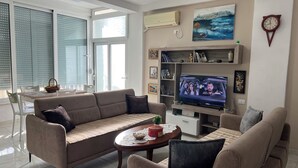 Ein modernes Wohnzimmer mit Sofa, Couchtisch, Fernseher und Essbereich mit Stühlen und Tisch.