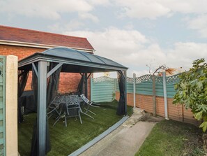 Ein überdachter Patio-Bereich mit Tisch und Stühlen, einer Backsteinmauer und einem Holzzaun.