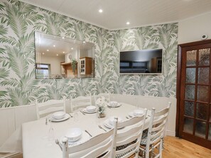 Comedor con un espejo grande, un televisor montado en la pared y una mesa de comedor preparada para cuatro.