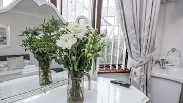 Un baño con lavabo blanco, espejo y un florero con flores blancas sobre una mesa blanca.