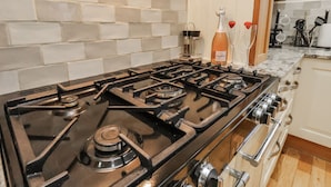 Una cucina con piano cottura a gas, zoccolo a parete rivestito di piastrelle bianche ed elettrodomestici in acciaio inossidabile.