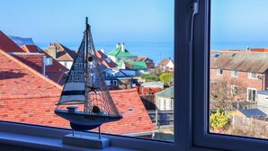 Ein Modellsegelboot auf einem Fensterbrett mit Blick auf Häuser und das Meer.