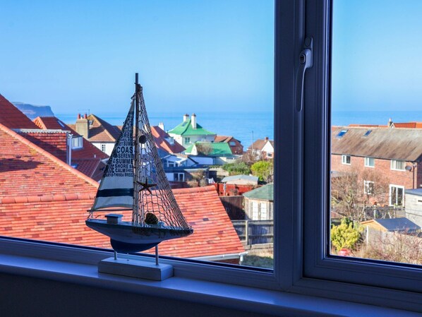 Ein Modellsegelboot auf einem Fensterbrett mit Blick auf Häuser und das Meer.