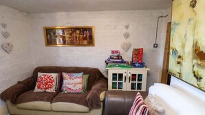 Ein Wohnzimmer mit einem braunen Sofa, einem weißen Sessel, einem gemusterten Teppich, einer Vitrine mit Büchern und einem Bild an der Wand.