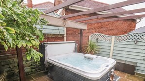 Ein Whirlpool in einem Garten mit einer Ziegelmauer, einer Holzpergola und einem Metallzaun.