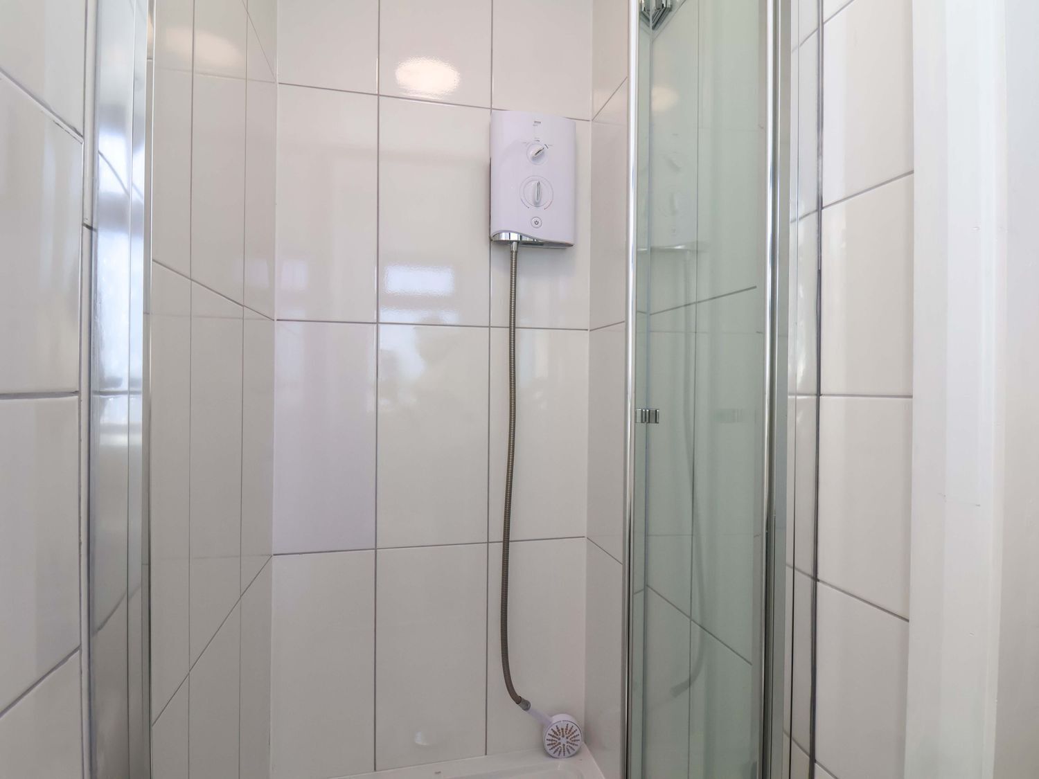 A shower with a glass enclosure, a control panel, and a handheld showerhead.