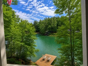 Eine Holzstege mit Stühlen, ein freier Blick auf einen von Bäumen umgebenen See und eine amerikanische Flagge.