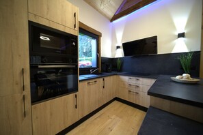 A modern kitchen with wooden cabinets, a built-in oven, a sink, and a flat-screen TV mounted on the wall. - "LSN6" Chalet: Cozy & High-End Comfort with Sauna, Spa, Air Conditioning, Foosball, and Pool (Anould)