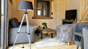 Una sala de estar acogedora con techo de madera, un sofá, una mesa de centro, una lámpara y un televisor.